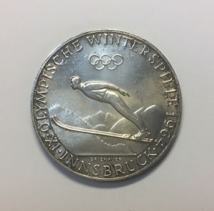 纪念币背部照片
背面设计：印有第九届冬季奥运会1964因斯布鲁克。上面是奥运五环，中为跳台滑雪男运动员飞翔雄姿，雪山为背景。
