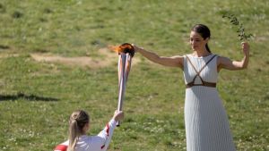 第一棒火炬手、希腊射击奥运冠军安娜·克拉卡奇（左）与扮演最高女祭司的演员乔治乌（右）交接圣火